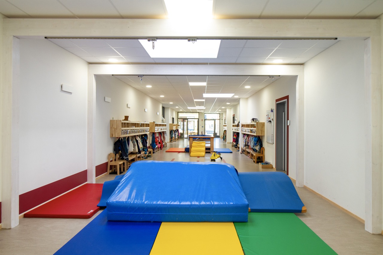 Kita Wirbelwind - Bewegungshalle Turnbereich mit bunten Matten, Kletterelementen und Kinder-Garderoben.
