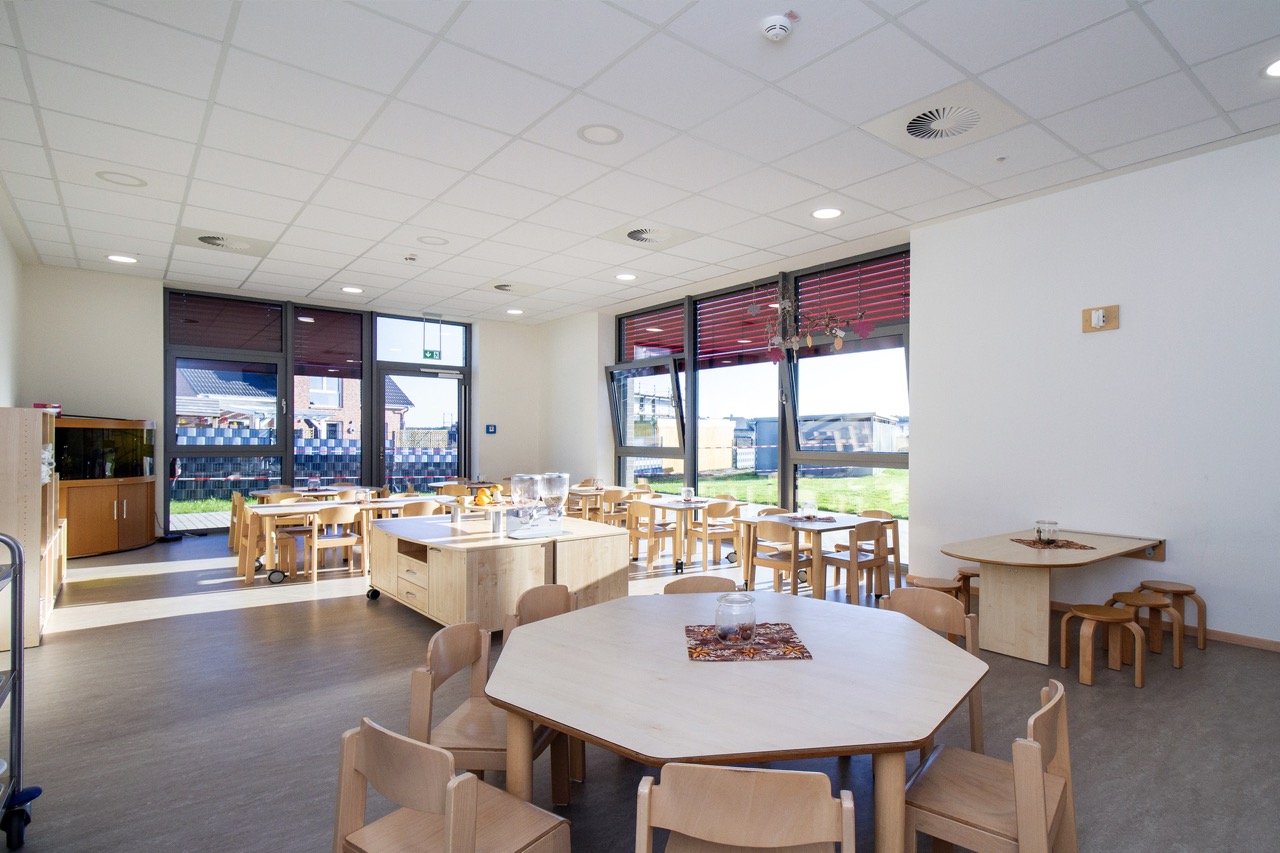 Kita Wirbelwind - Cafeteria Kinder-Speiseraum mit kleinen Holztischen, Stühlen und großen Fenstern.